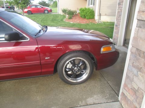 2004 Ford Crown Victoria - A red sedan is parked in a driveway, showing its front quarter panel and custom wheels.