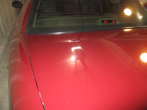 2004 Ford Crown Victoria - Close-up of a red car's trunk lid shows minor imperfections and reflections.
