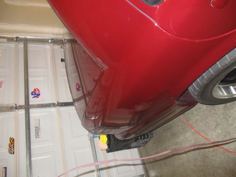 2004 Ford Crown Victoria - Close-up of a red car's rear quarter panel and tire, viewed from a low angle in a garage.