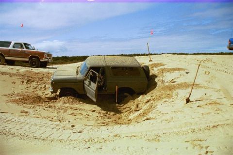 1979 Ford Bronco - This vehicle appears to be stuck in the sand with its door open, while another vehicle waits nearby.