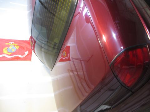 2004 Ford Crown Victoria - Rear view of a red car with US Marine Corps flags visible.