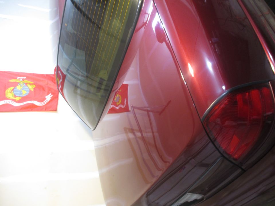 Red car's rear quarter panel and taillight with US Marine Corps flags in background