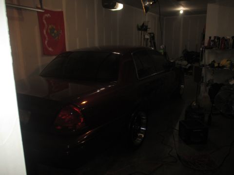 2004 Ford Crown Victoria - A dark red 2004 Ford Crown Victoria sedan is parked in a dimly lit garage.