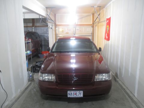 2004 Ford Crown Victoria - A maroon 2004 Ford Crown Victoria is parked in a garage, with another vehicle visible in the background.