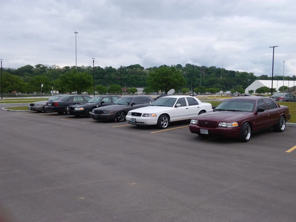 Maroon Ford Crown Victoria parked in a lot, front 3/4 view, with other Crown Victorias behind it