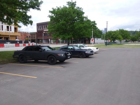 2004 Ford Crown Victoria - Three police-style sedans, including a black one, are parked in a lot. The registry claims the black car is a 2004 Ford Crown Victoria.