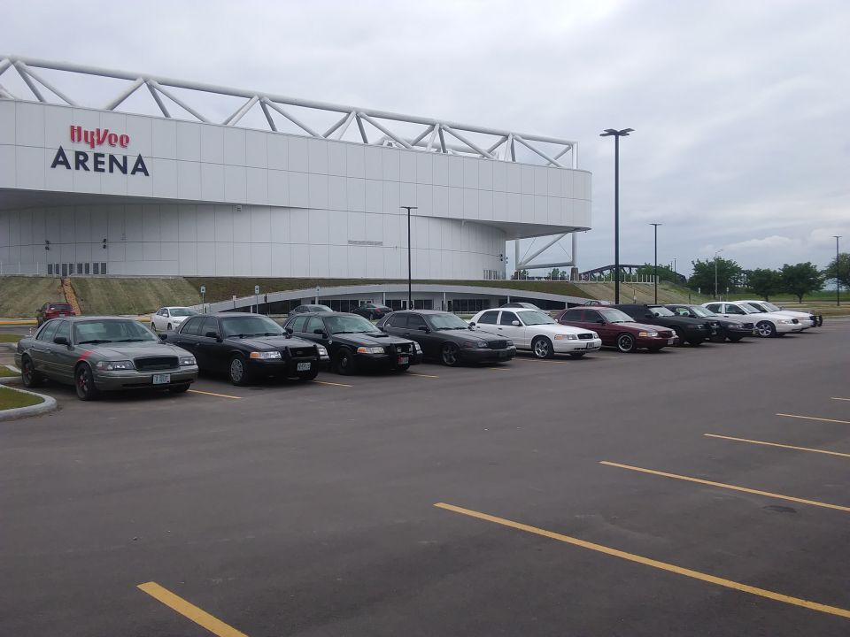 Several Ford Crown Victoria sedans, some appearing to be police interceptors, parked in a lot in front of the Hy-Vee Arena