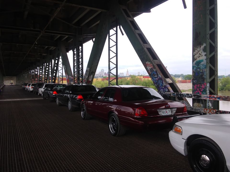 Maroon 2004 Ford Crown Victoria, rear view, on a bridge, with other cars in line