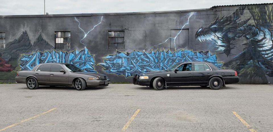 Two Ford Crown Victorias parked in front of a mural of a dragon and abstract art
