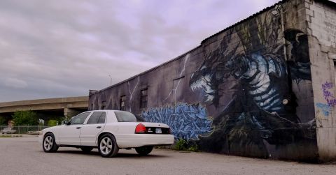 2004 Ford Crown Victoria - A white 2004 Ford Crown Victoria is parked in front of a building with a large dragon mural.