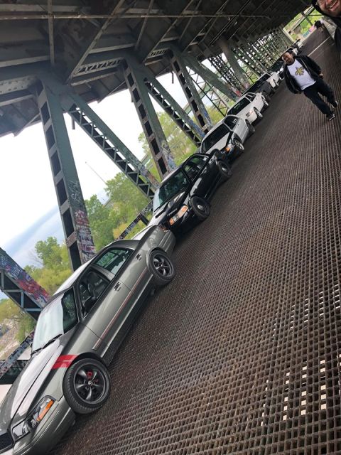 2004 Ford Crown Victoria - Several sedans, including a gray 2004 Ford Crown Victoria, are lined up on a metal-grate bridge.