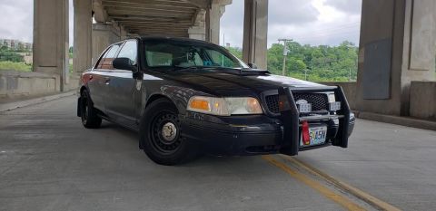 2004 Ford Crown Victoria - A black 2004 Ford Crown Victoria, equipped with a push bar, is seen from a three-quarter front angle under a bridge.