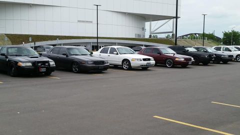 2004 Ford Crown Victoria - A lineup of Ford Crown Victoria sedans are parked in a lot outside a large building.
