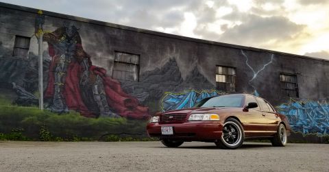 2004 Ford Crown Victoria - A maroon sedan is parked in front of a large mural depicting a warrior and abstract art.
