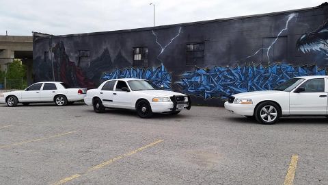 2004 Ford Crown Victoria - Three white Ford Crown Victorias are parked in a lot, with a mural on the wall behind them.