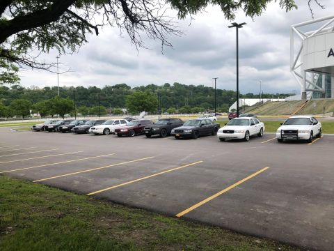 2004 Ford Crown Victoria - A group of sedans, including several police cruisers, are parked in an outdoor lot under a cloudy sky.