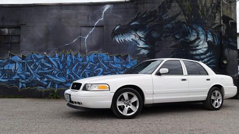 2004 Ford Crown Victoria - A white 2004 Ford Crown Victoria is parked in front of a building with a large dragon mural.