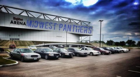 2004 Ford Crown Victoria - Several Ford Crown Victorias are parked in a lot in front of the Hy-Vee Arena under a dramatic sky.