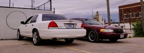 2004 Ford Crown Victoria - Two Ford Crown Victorias are parked next to each other on a cloudy day.