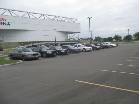 2004 Ford Crown Victoria - Multiple Ford Crown Victorias are parked in a lot outside a large arena.