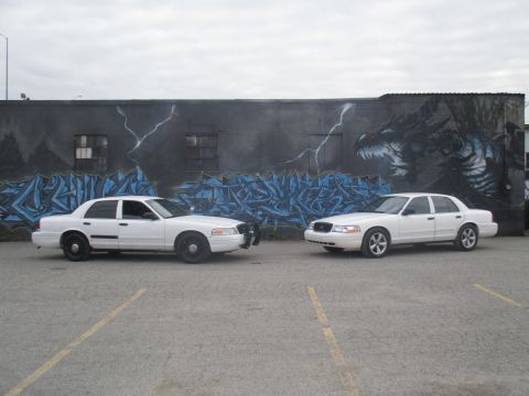 2004 Ford Crown Victoria - Two white Ford Crown Victorias are parked in front of a mural depicting a dragon and lightning.