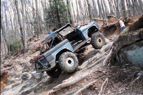 1976 Ford Bronco - Modified 1976 Ford Bronco navigating a steep, rocky trail in a wooded area.