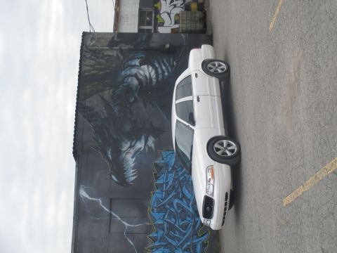 2004 Ford Crown Victoria - A white sedan is parked in front of a building with a large mural on its side.