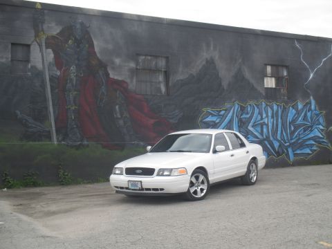 2004 Ford Crown Victoria - A white 2004 Ford Crown Victoria is parked in front of a building with a large mural.