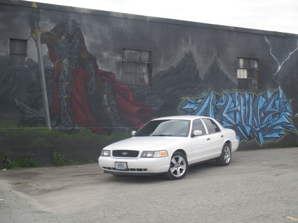 White 2004 Ford Crown Victoria parked in front of a mural of a knight and graffiti