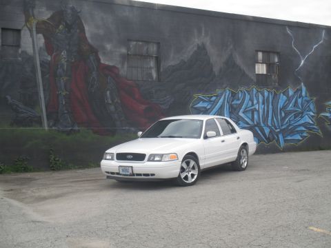 2004 Ford Crown Victoria - A white Ford Crown Victoria sedan is parked in front of a building with graffiti art.