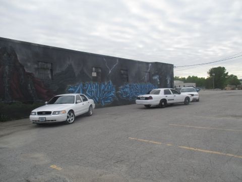 2004 Ford Crown Victoria - Two white Ford Crown Victorias are parked in front of a building with a large mural.