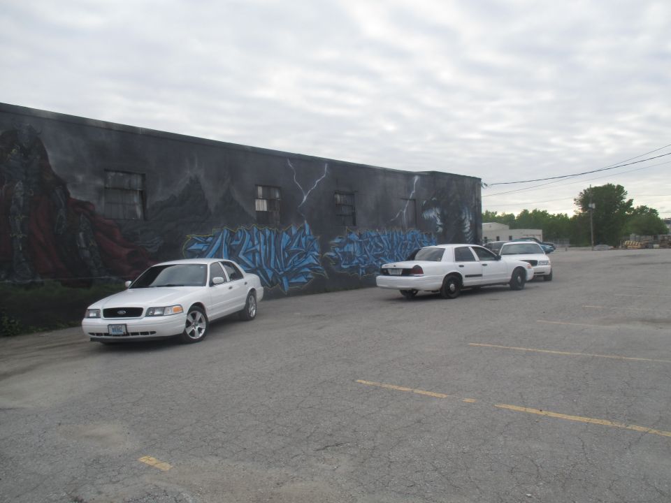 White 2004 Ford Crown Victoria parked in front of a graffitied wall