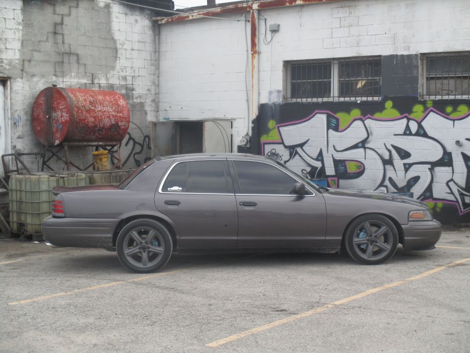Gray Ford Crown Victoria parked in front of a graffiti-covered wall