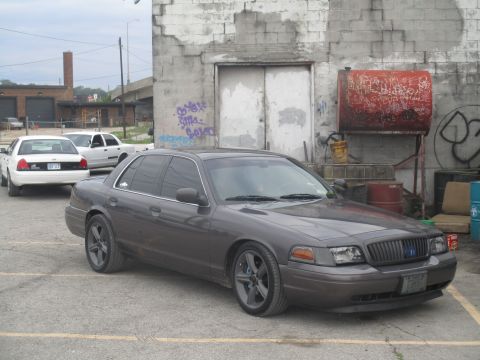 2004 Ford Crown Victoria - A row of Ford Crown Victorias are parked outside a weathered building with graffiti.