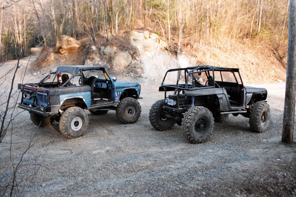 Two lifted topless early Ford Bronco rock crawlers parked on gravel