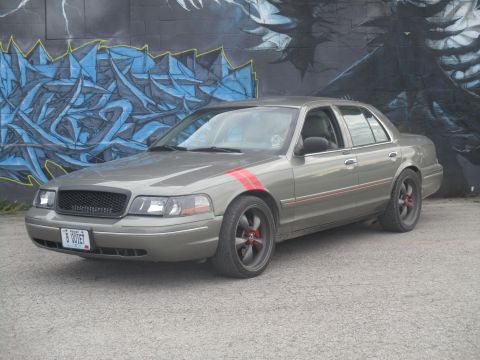 2004 Ford Crown Victoria - This gray sedan features red racing stripes on the front fender and along the door trim, paired with a blacked-out grille and aftermarket w…