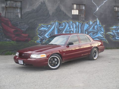 2004 Ford Crown Victoria - Maroon 2004 Ford Crown Victoria parked in front of a graffiti-covered wall.