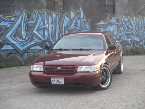 2004 Ford Crown Victoria - Maroon Ford Crown Victoria with custom wheels parked in front of a graffiti-covered wall.