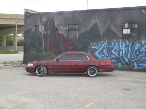 2004 Ford Crown Victoria - A maroon 2004 Ford Crown Victoria is parked in front of a building with a mural and graffiti art.