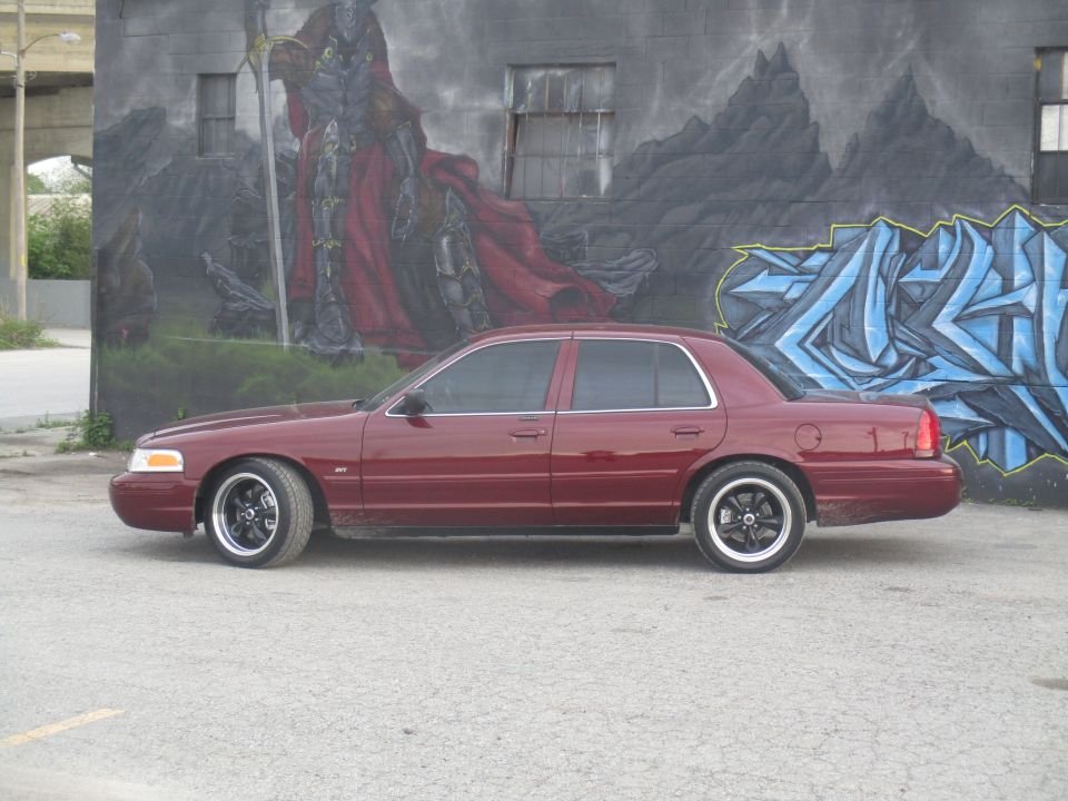 Maroon sedan parked in front of a mural, side view. Aftermarket wheels are visible
