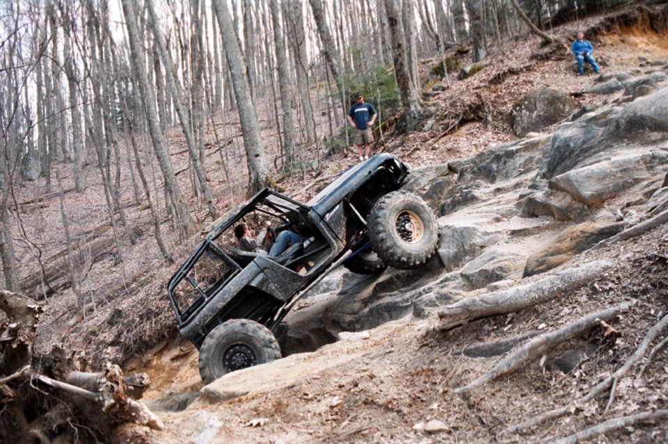 Black caged rock-crawler 4x4 climbing steep rock ledge in bare winter woods