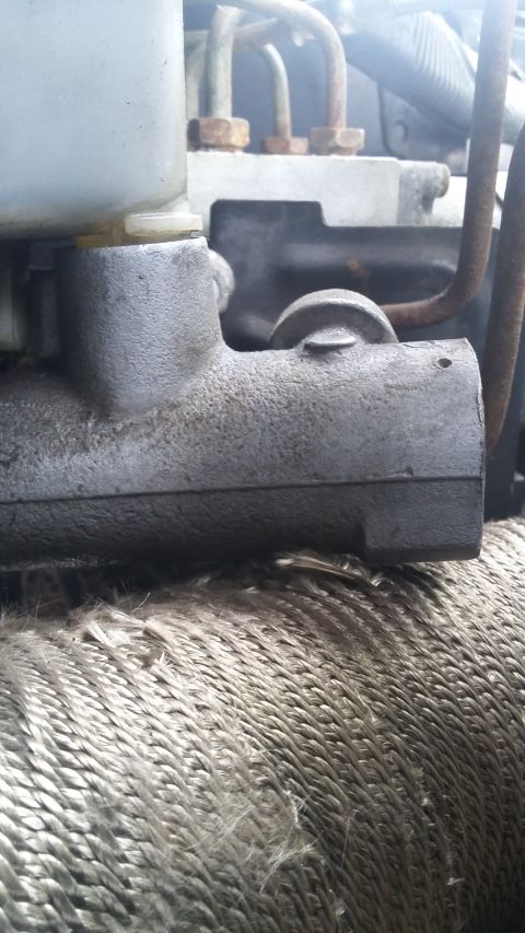 close-up of a brake master cylinder with hoses and engine block in background