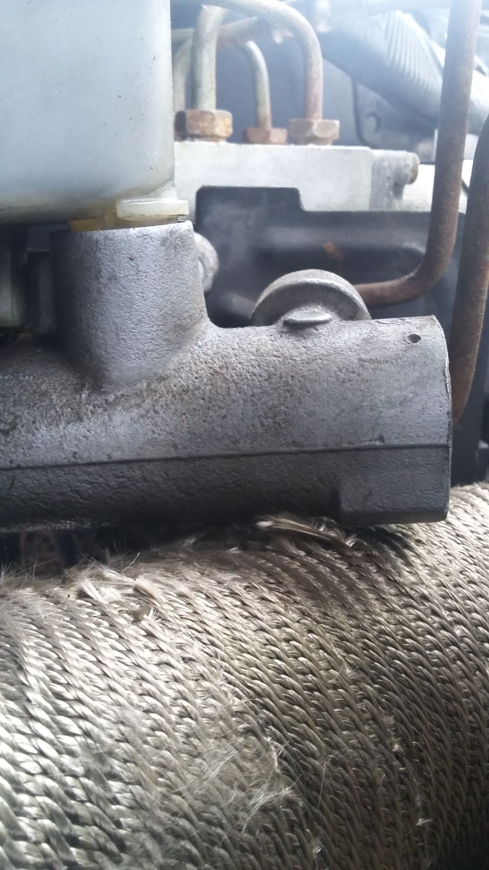 close-up of a brake master cylinder with hoses and engine block in background