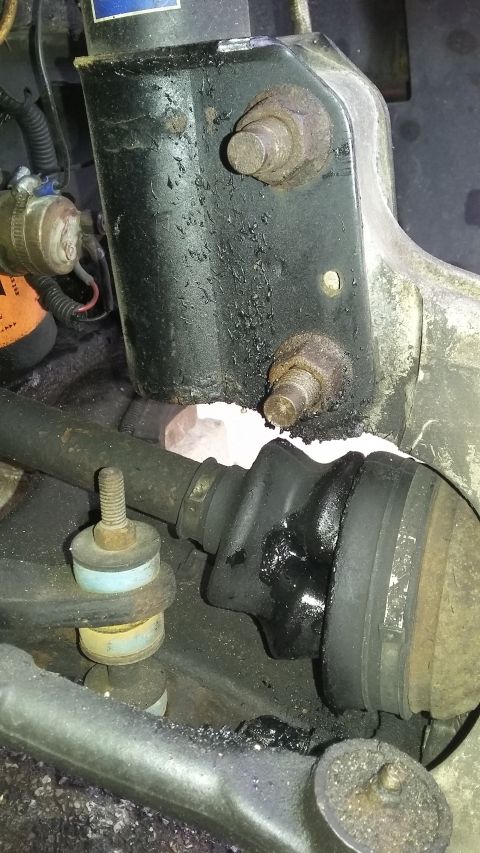 Close-up of a greasy CV joint boot, strut mount, and suspension linkage