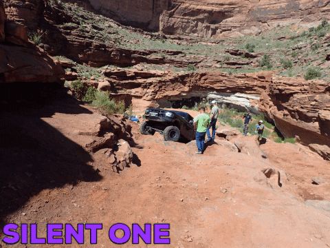 1995 Ford Bronco - An off-road vehicle is parked on a dirt path within a canyon, with text visible on the ground.