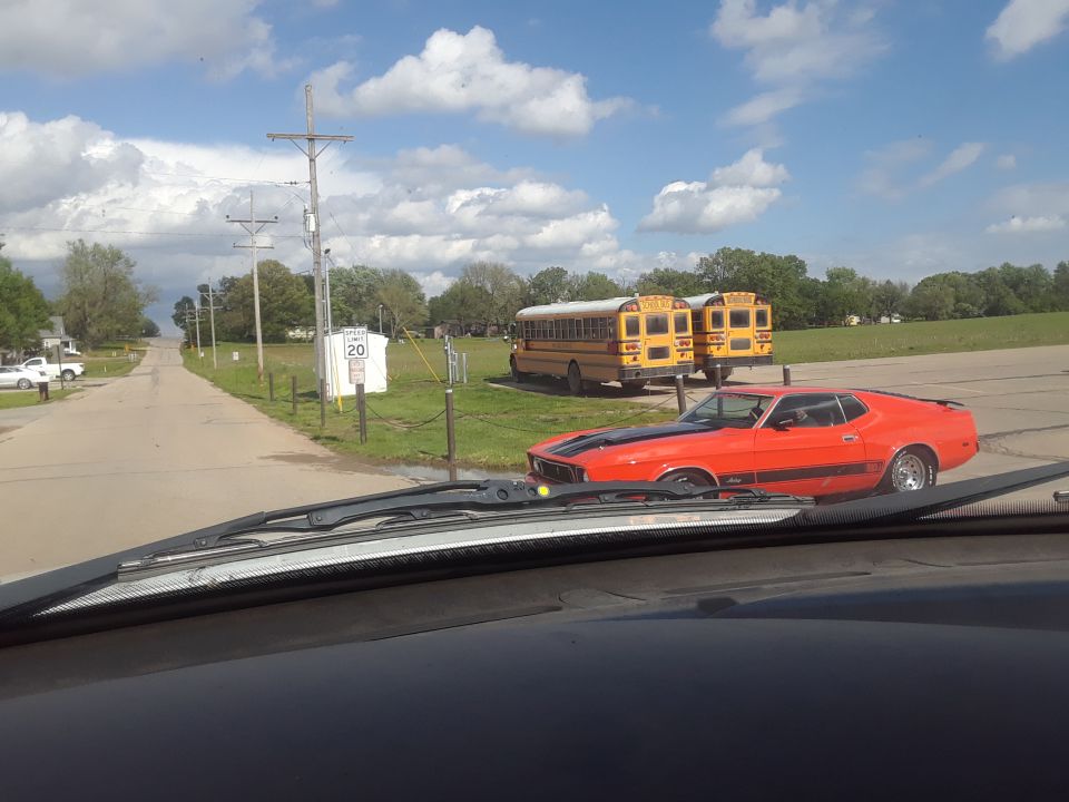 Orange 1971 Ford Mustang Mach 1 parked near two yellow school buses