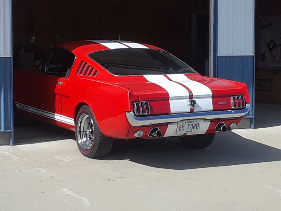 Red 1965 Ford Mustang fastback with white stripes parked in a garage