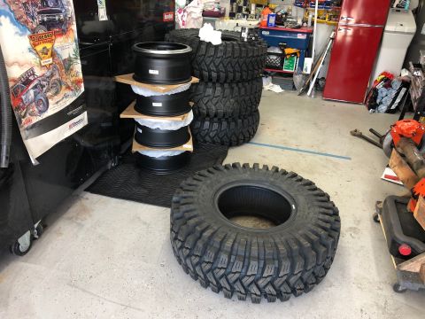 1992 Jeep Wrangler - Four black rims are stacked, with a large off-road tire in the foreground, in a garage setting.