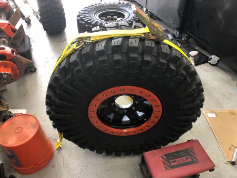 1992 Jeep Wrangler - Off-road tires and wheels are secured with a yellow strap in a workshop setting.