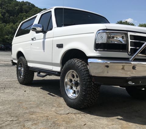 1995 Ford Bronco - This white Ford Bronco is shown from a three-quarter front view, highlighting its tires and side steps.